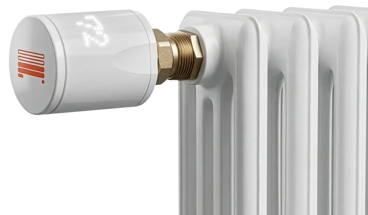 A white ARC unit threaded onto the brass valve of a white cast-iron radiator, a temperature lit on its display.